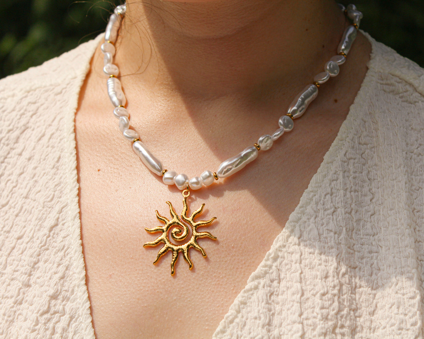 Necklace with sun pendant and pearl beads worn by a person