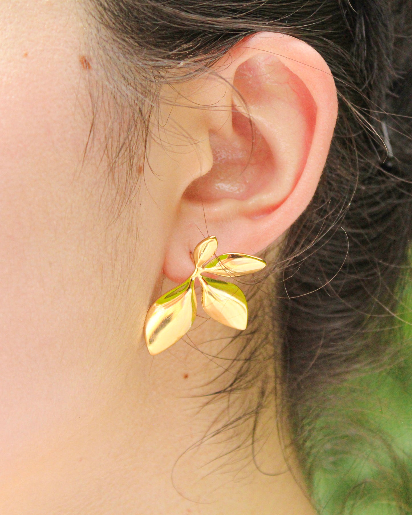 Gold leaf-shaped earring worn on an ear with a blurred background