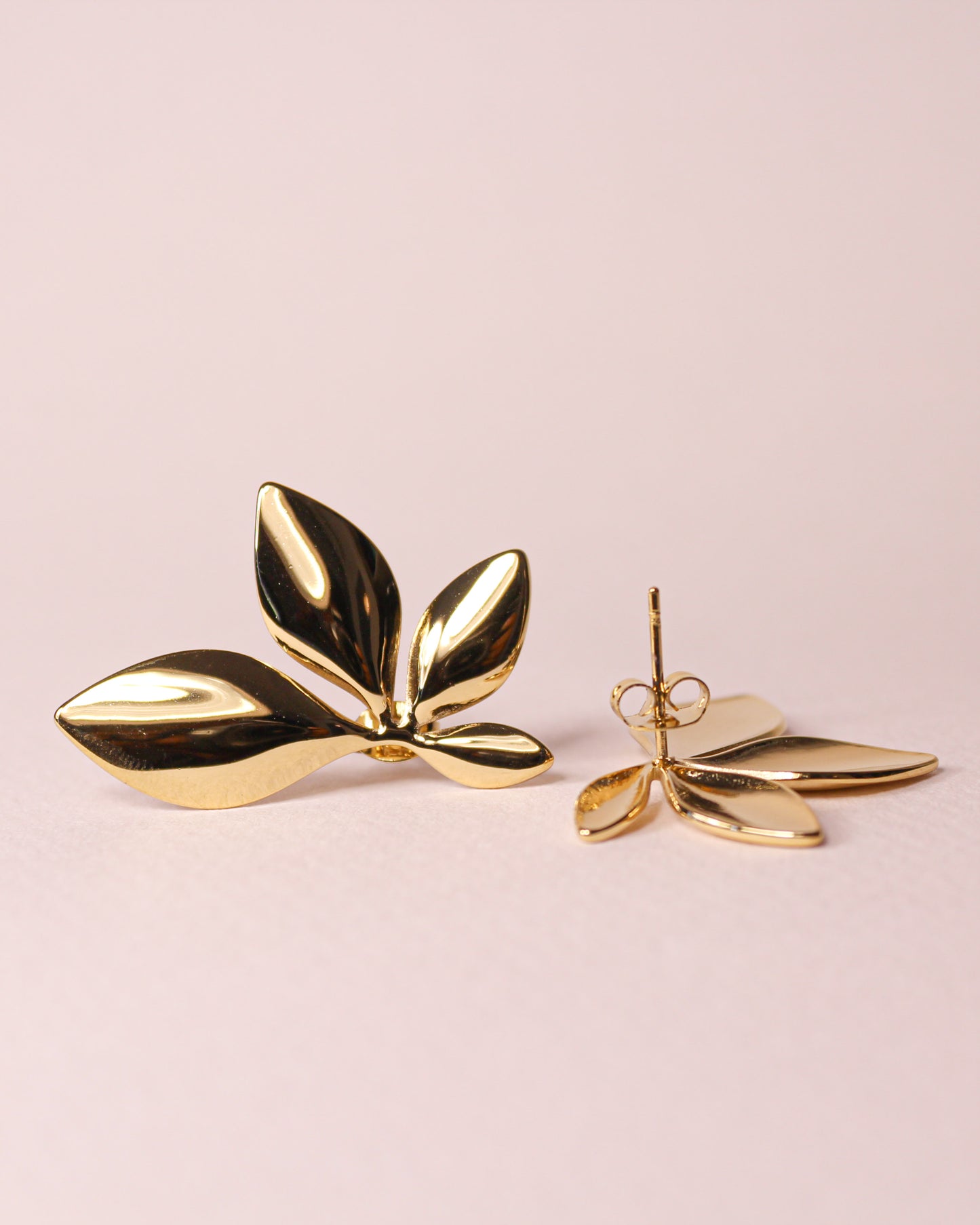 Gold leaf-shaped earrings on a light pink background