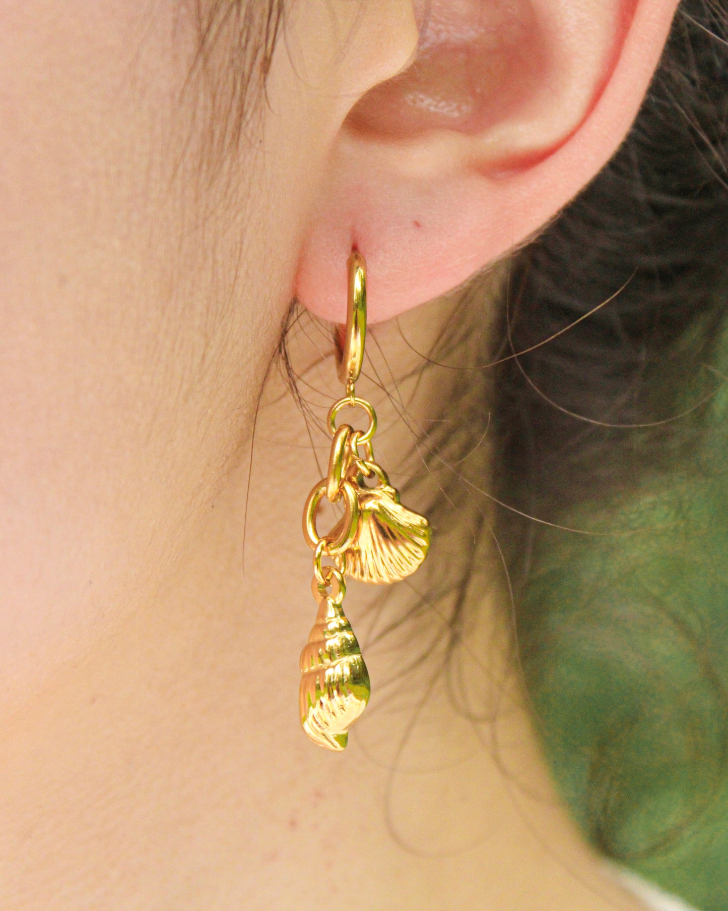 Gold earrings with shell charms worn by a person