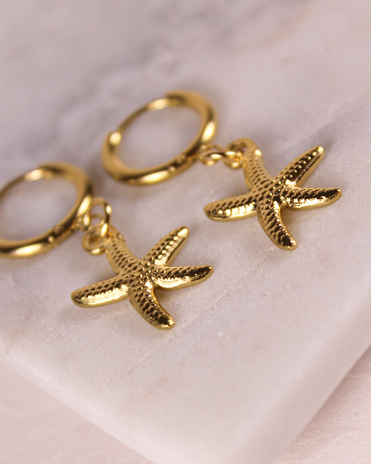 Gold starfish earrings on a light pink background
