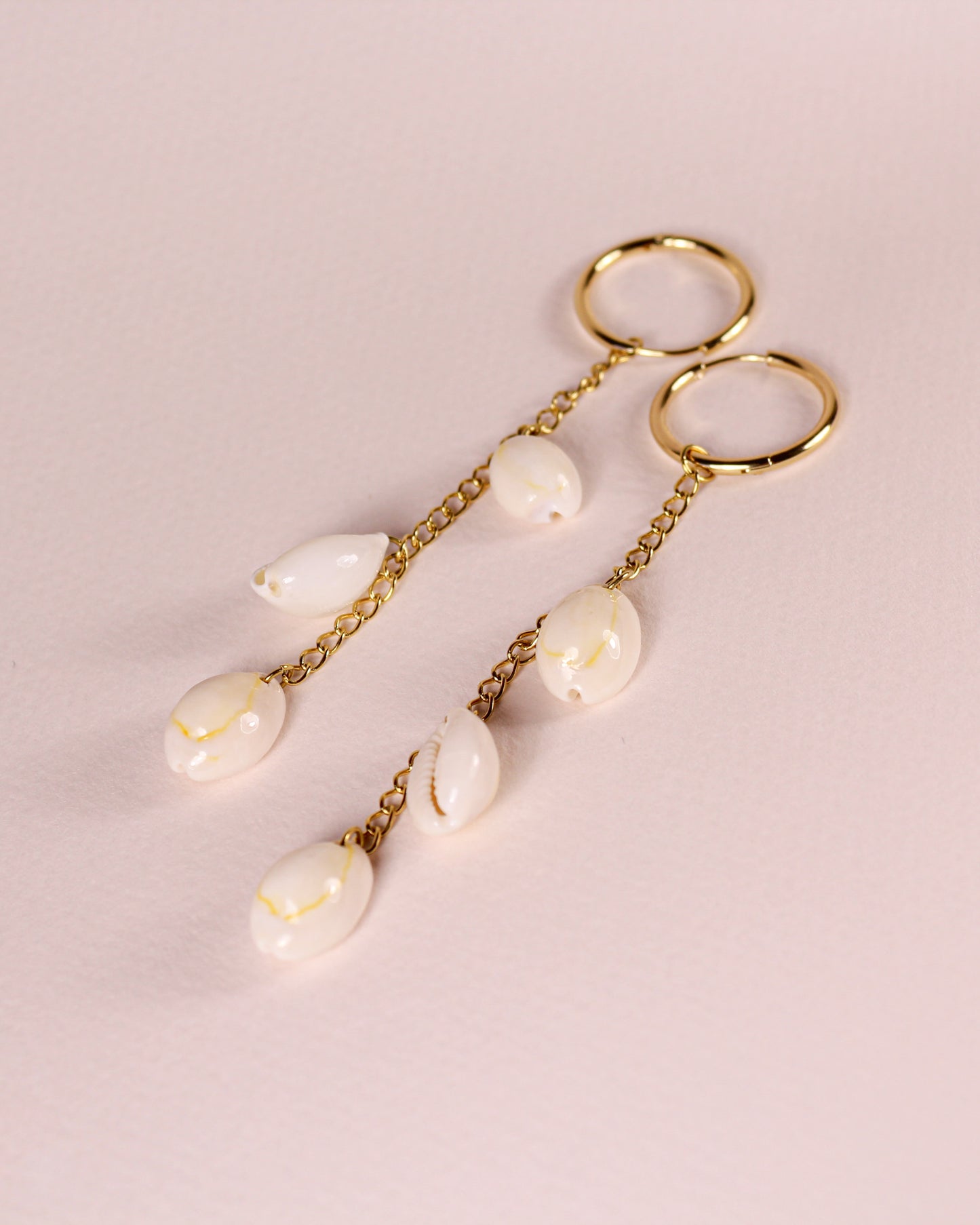Gold earrings with pearl-like beads on a light pink background