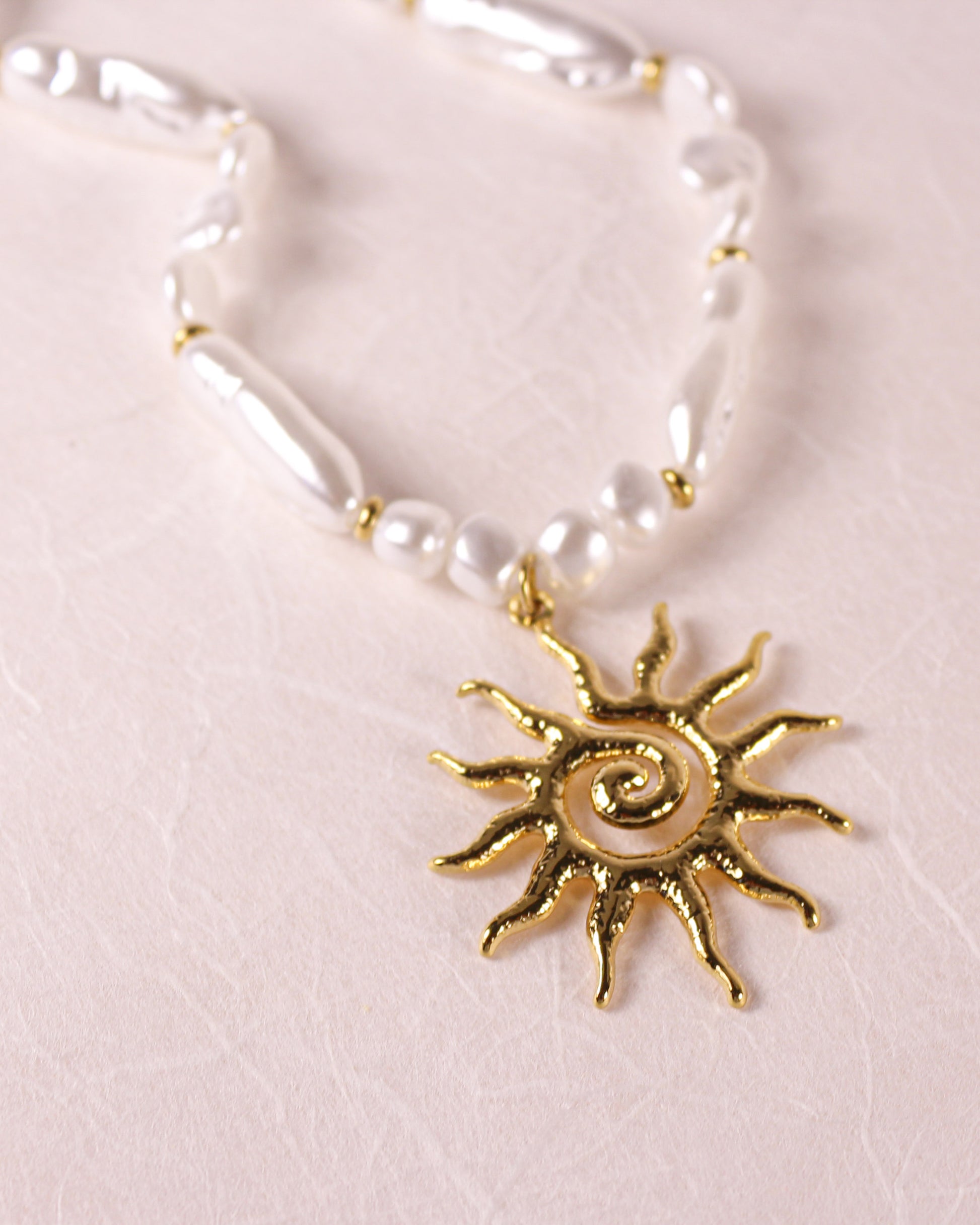 Necklace with a gold sun pendant on a light pink background