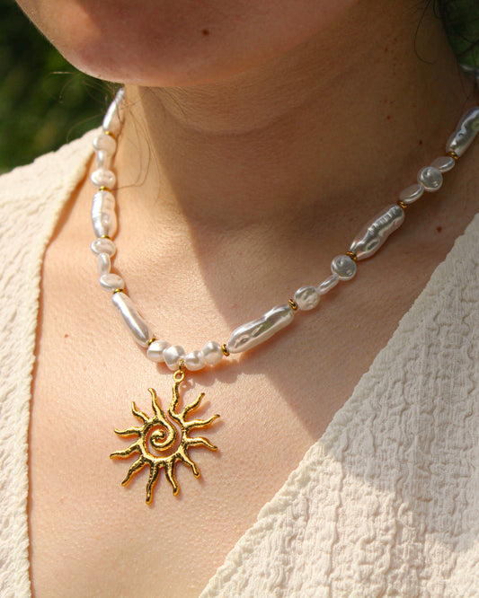 Necklace with sun pendant and pearl beads on a person wearing a light-colored top.