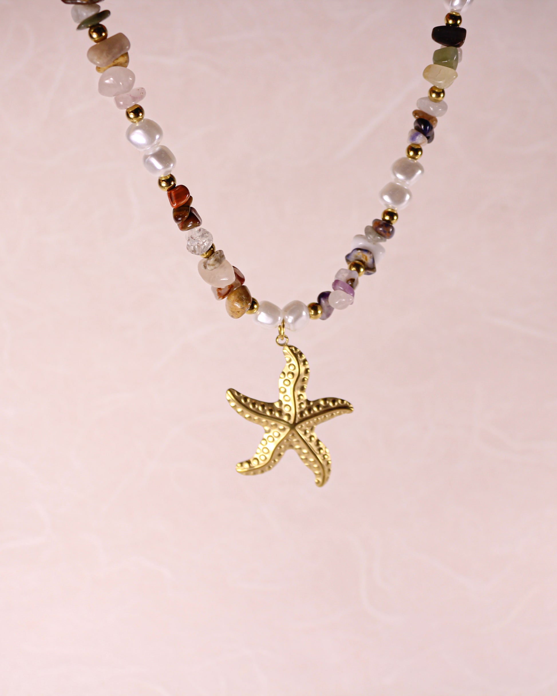Necklace with a gold starfish pendant on a light pink background