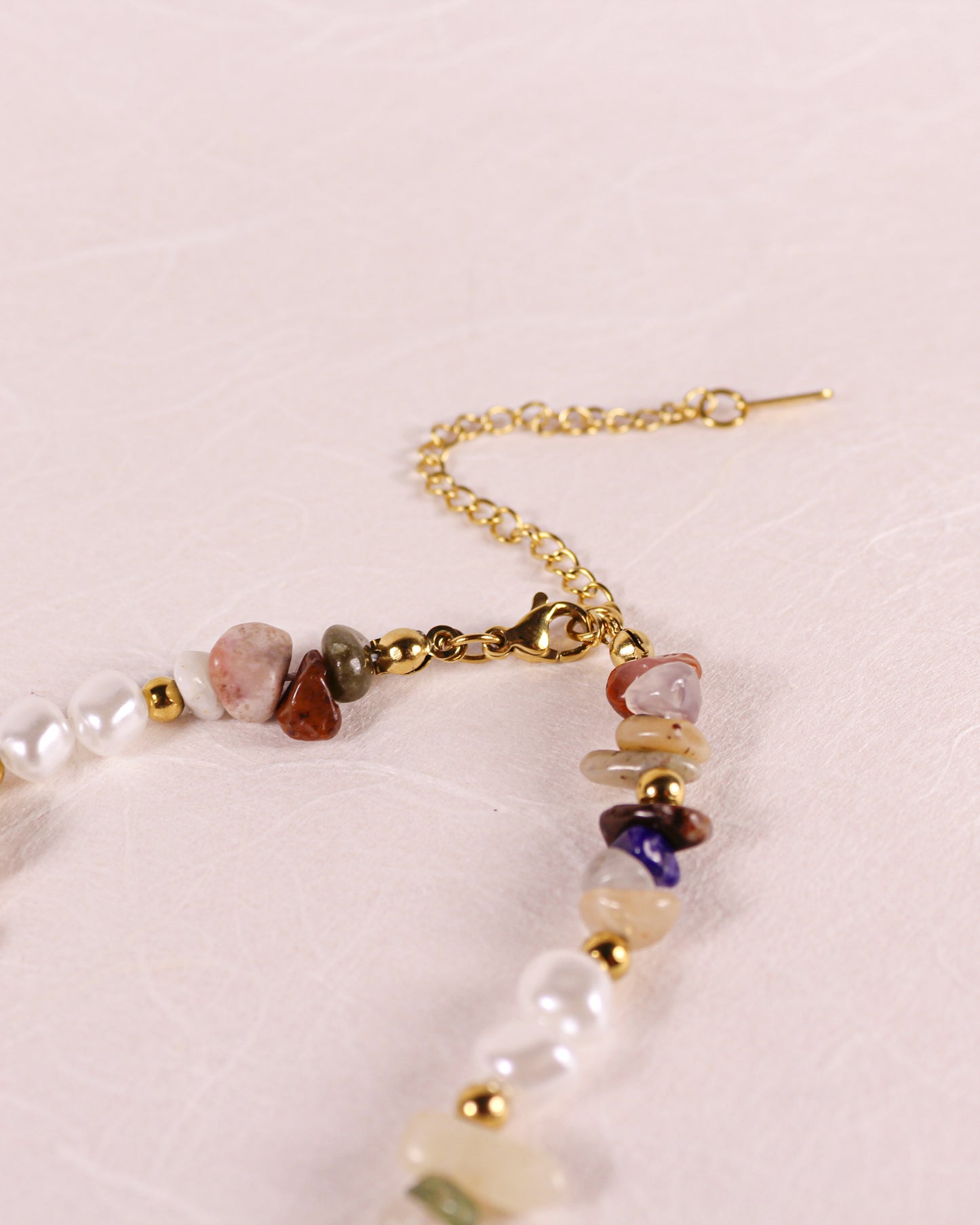 Necklace with pearls and multicolored stones on a light pink background