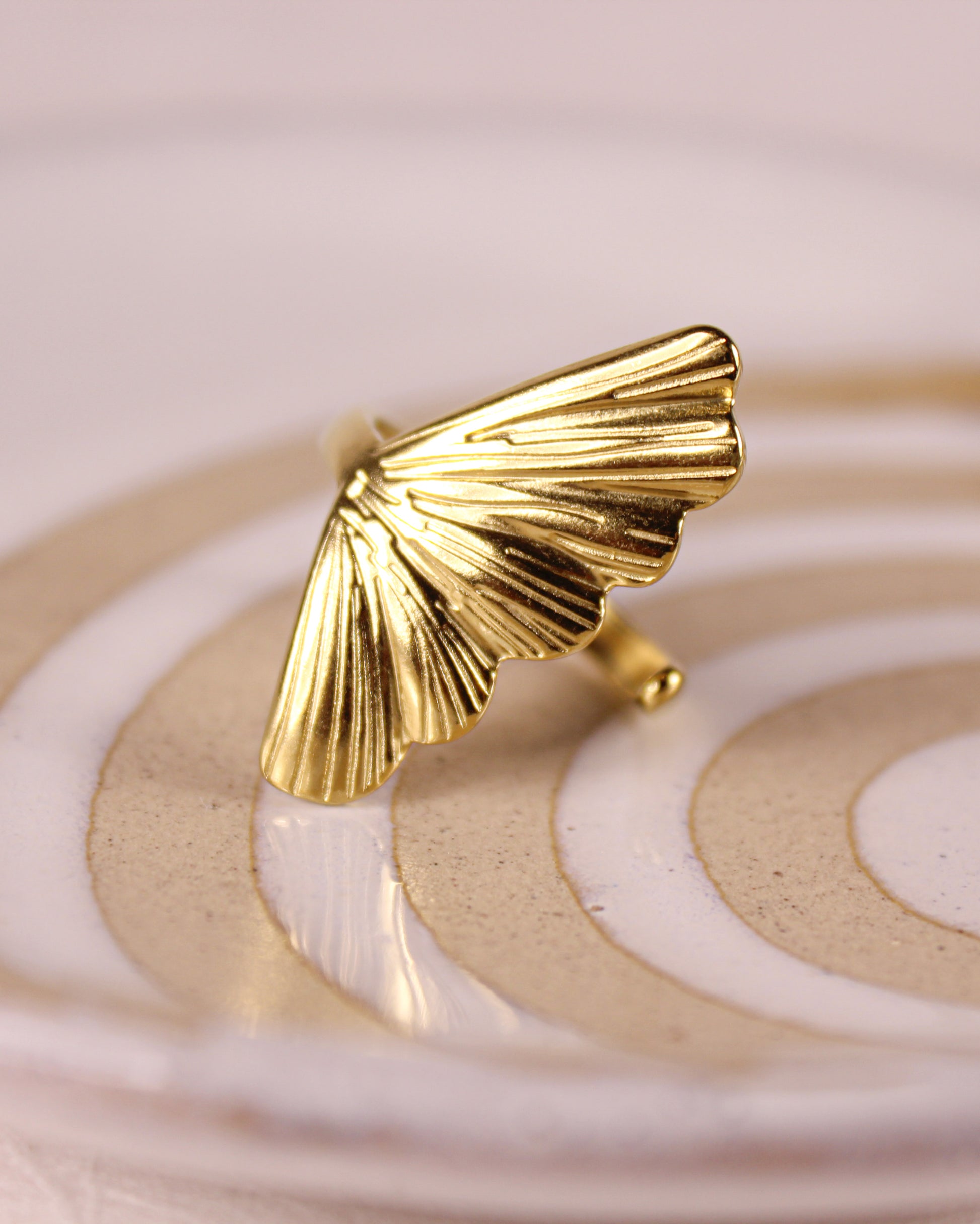 Gold leaf-shaped ring on a decorative stand with a soft pink background
