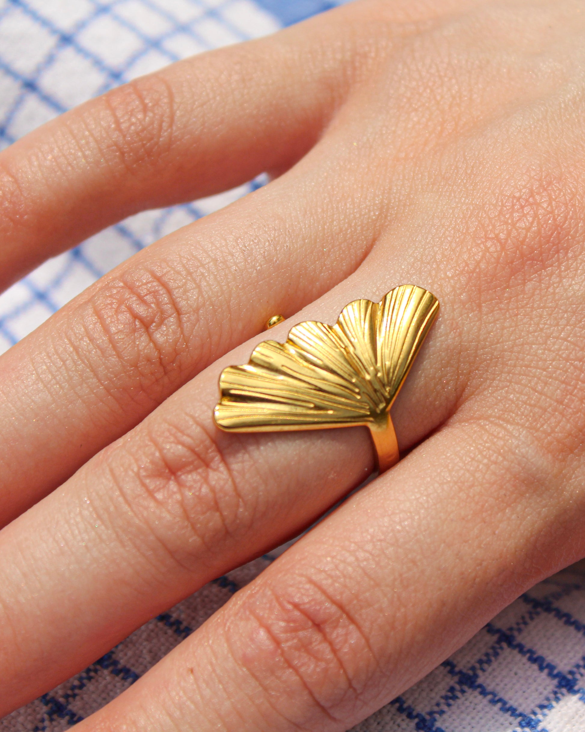 Gold fan-shaped ring on a finger with a checkered fabric background