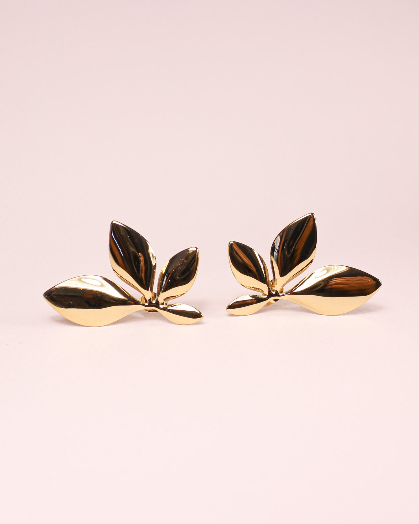 Gold leaf-shaped earrings on a light pink background