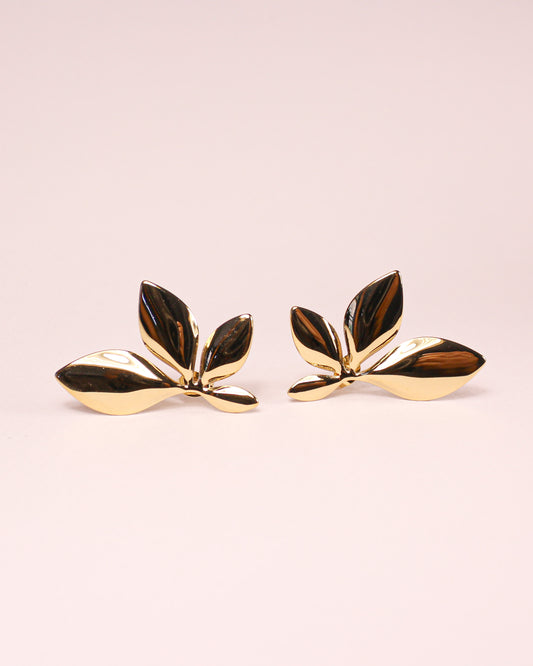 Gold leaf-shaped earrings on a light pink background