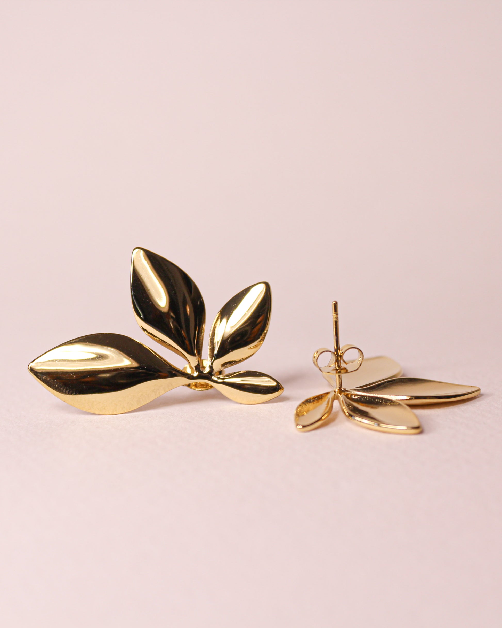 Gold leaf-shaped earrings on a light pink background
