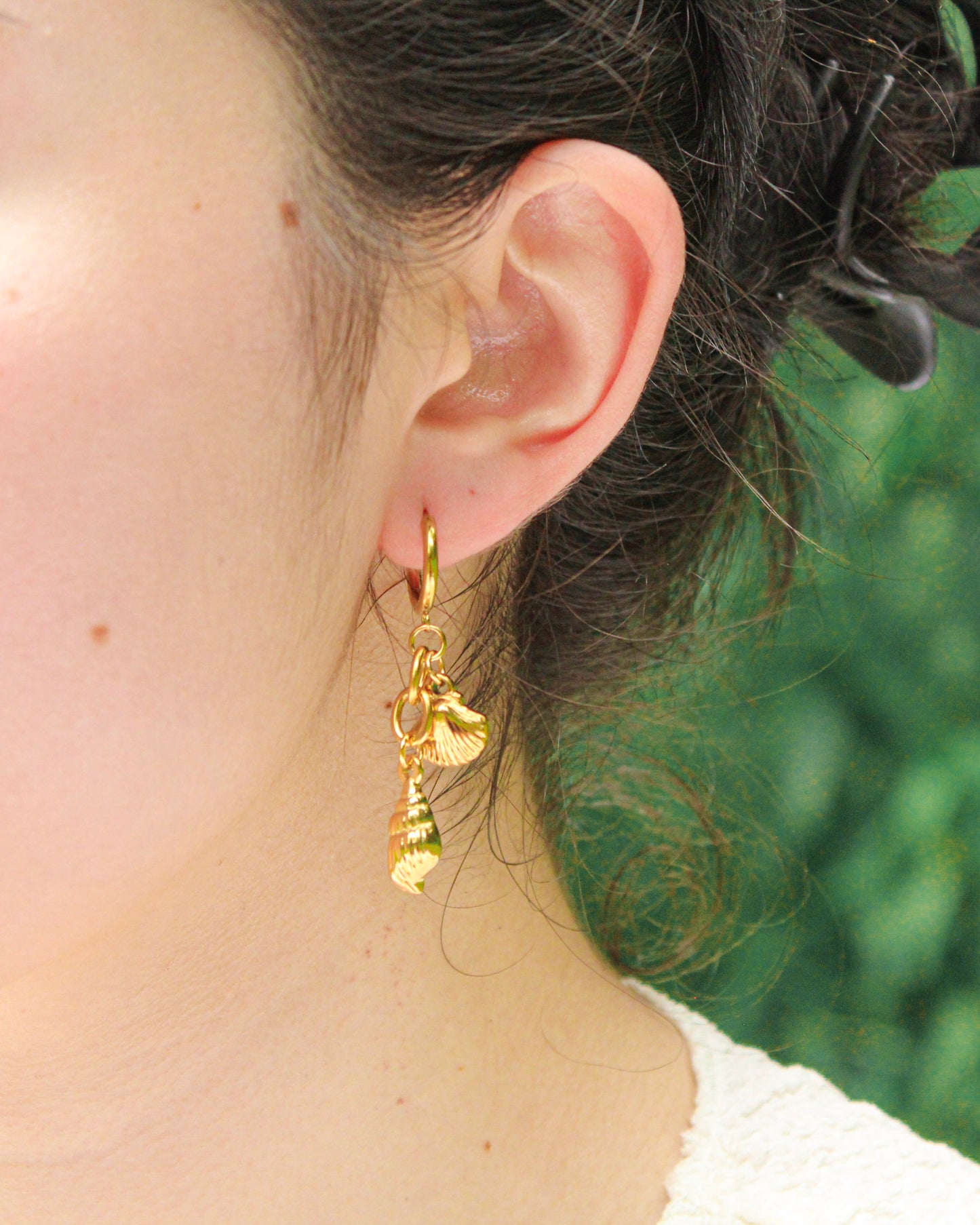 Gold hoop earrings with dangling charms worn by a person with blurred green background