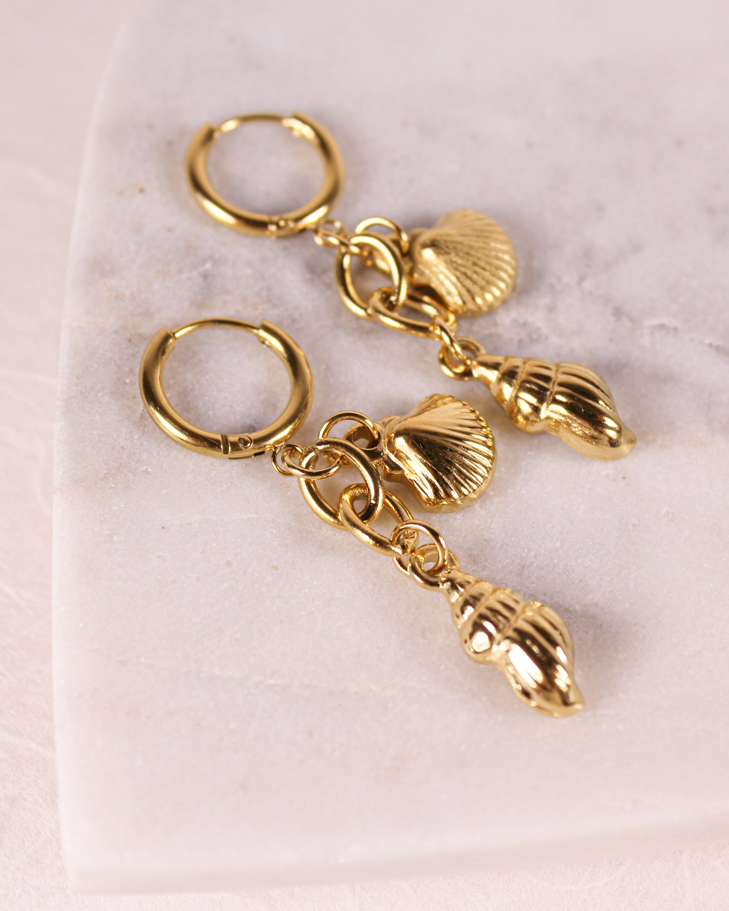 Gold earrings with shell charms on a light pink background