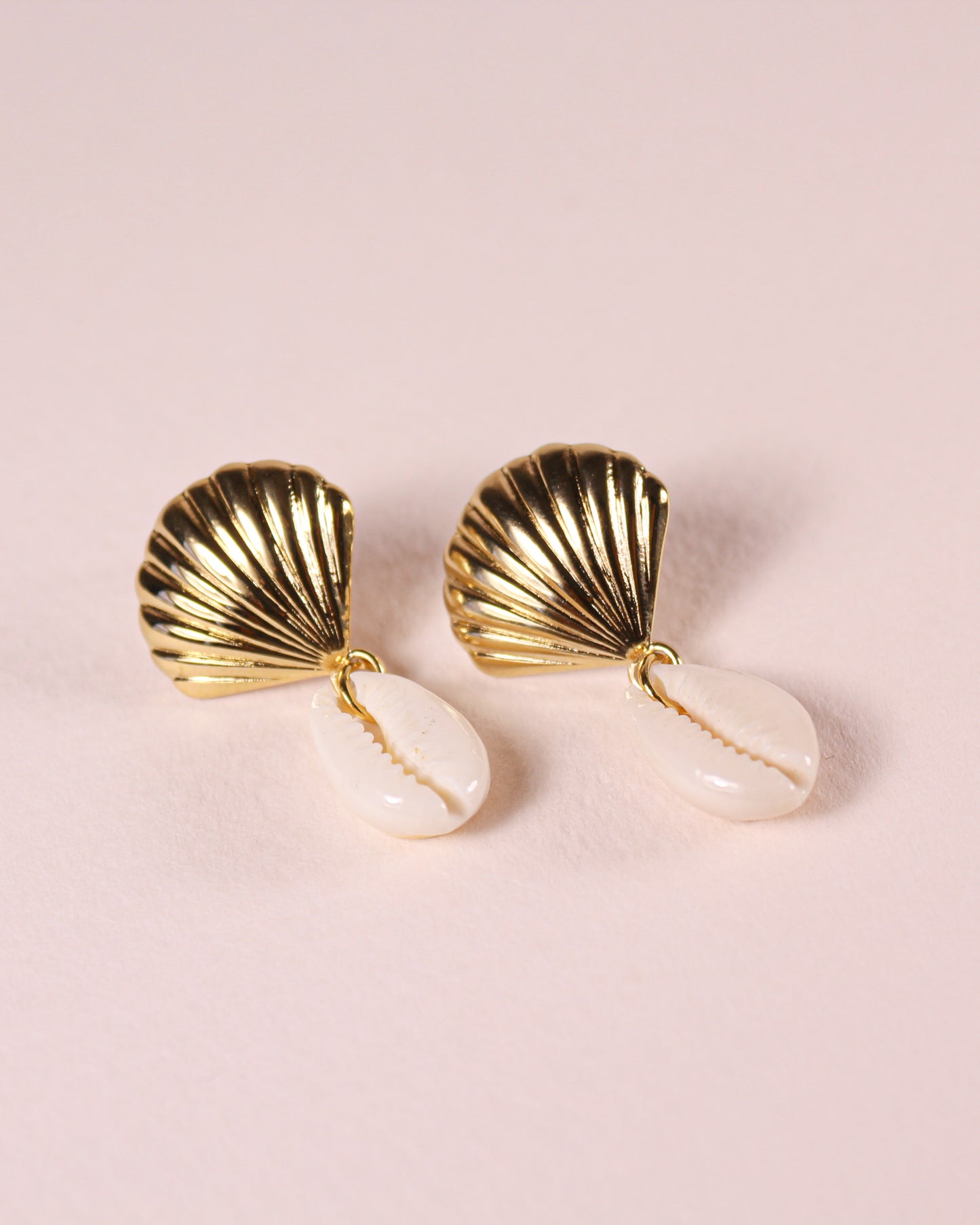 Gold shell-shaped earrings on a pink background