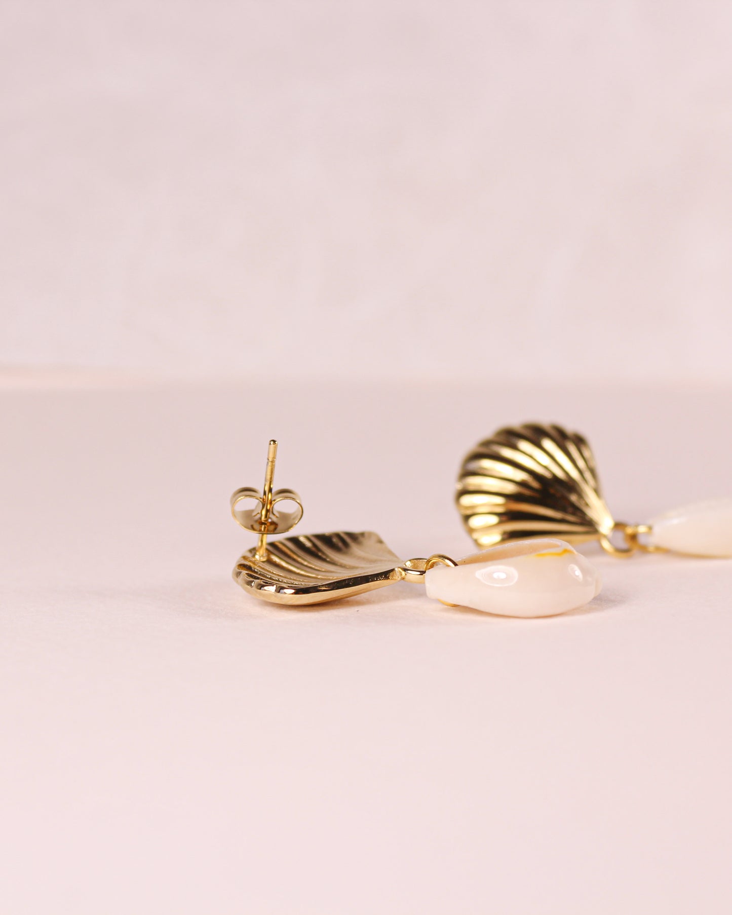 Gold and shell-shaped earrings on a light pink background