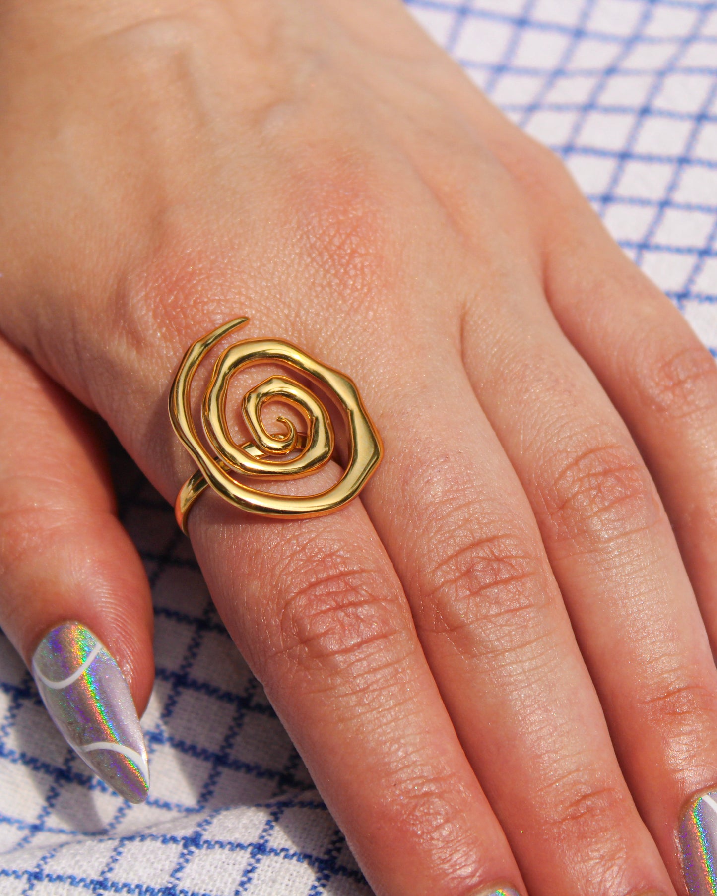 Gold spiral ring on a hand with a checkered fabric background