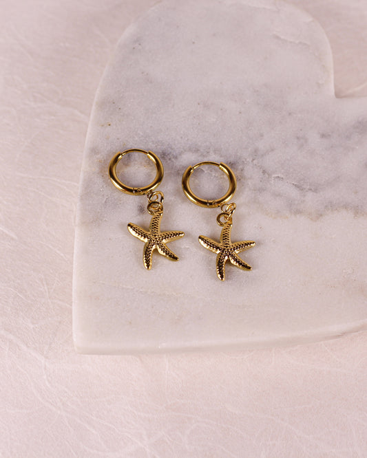 Gold hoop earrings with starfish charms on a marble surface