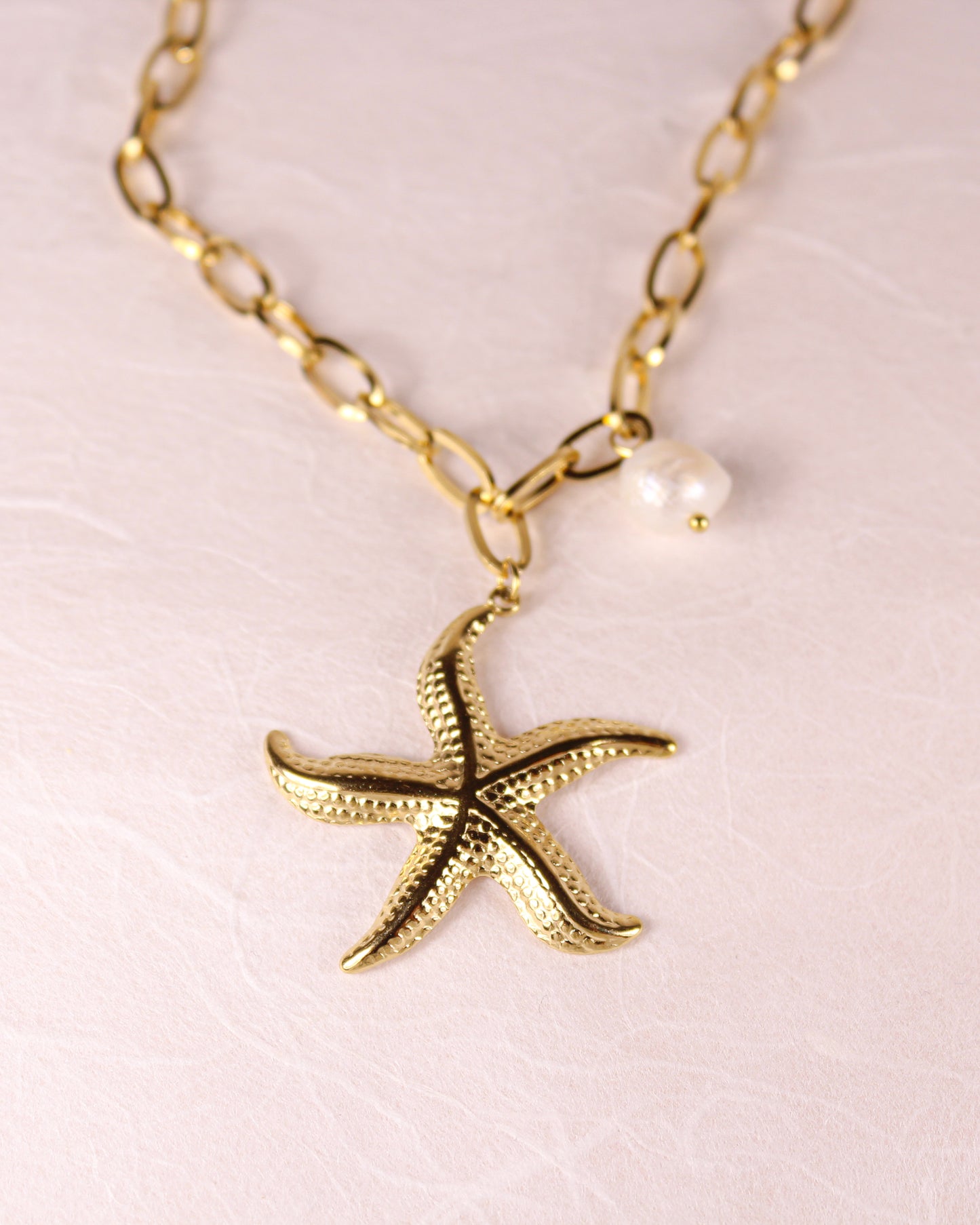 Gold starfish pendant necklace with a pearl on a light pink background