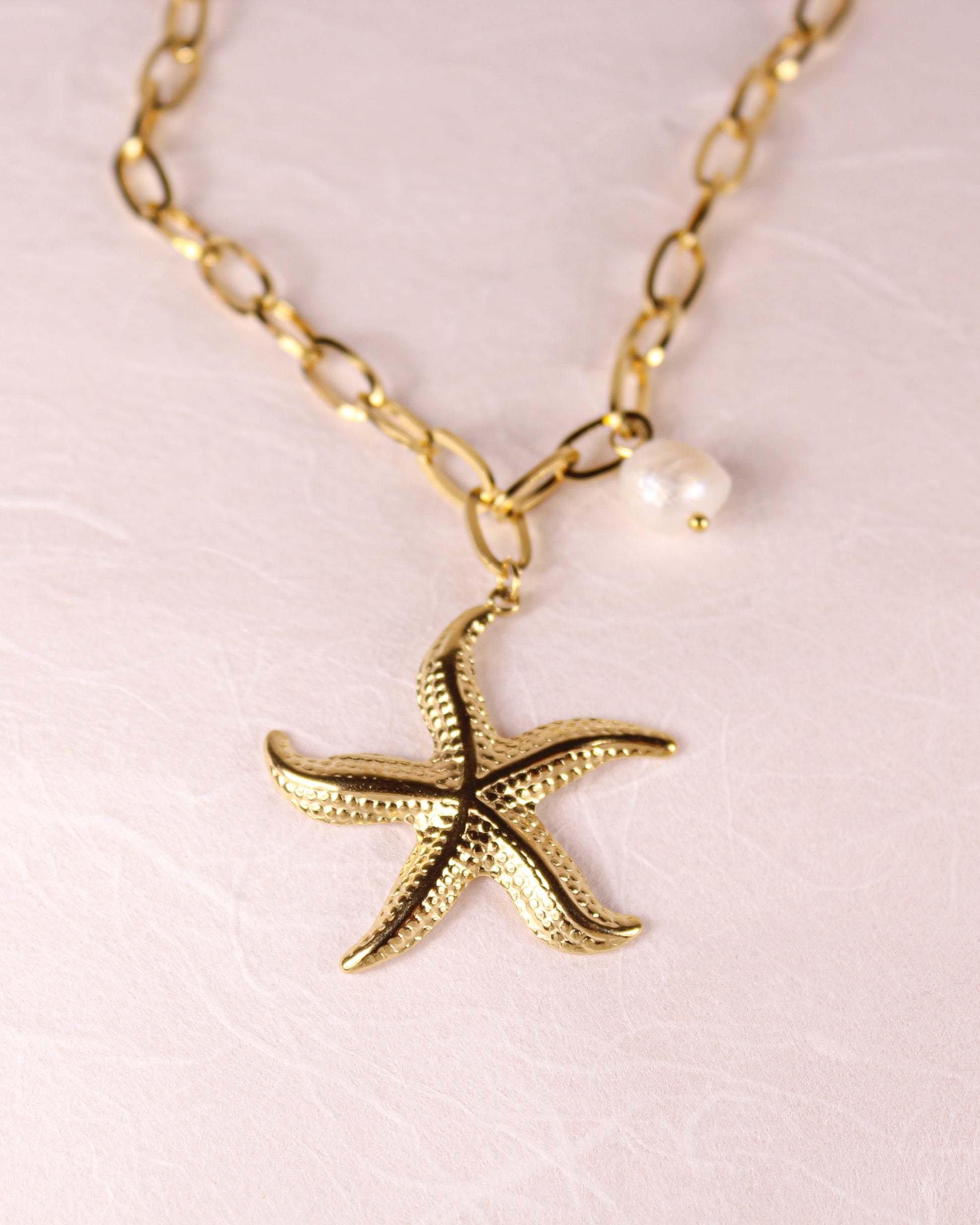 Gold starfish pendant necklace with a pearl on a light pink background