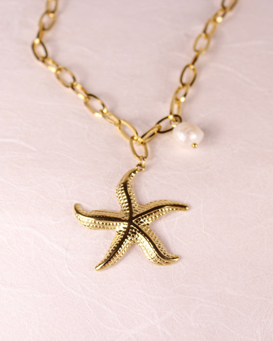Gold starfish pendant necklace with a pearl on a light pink background