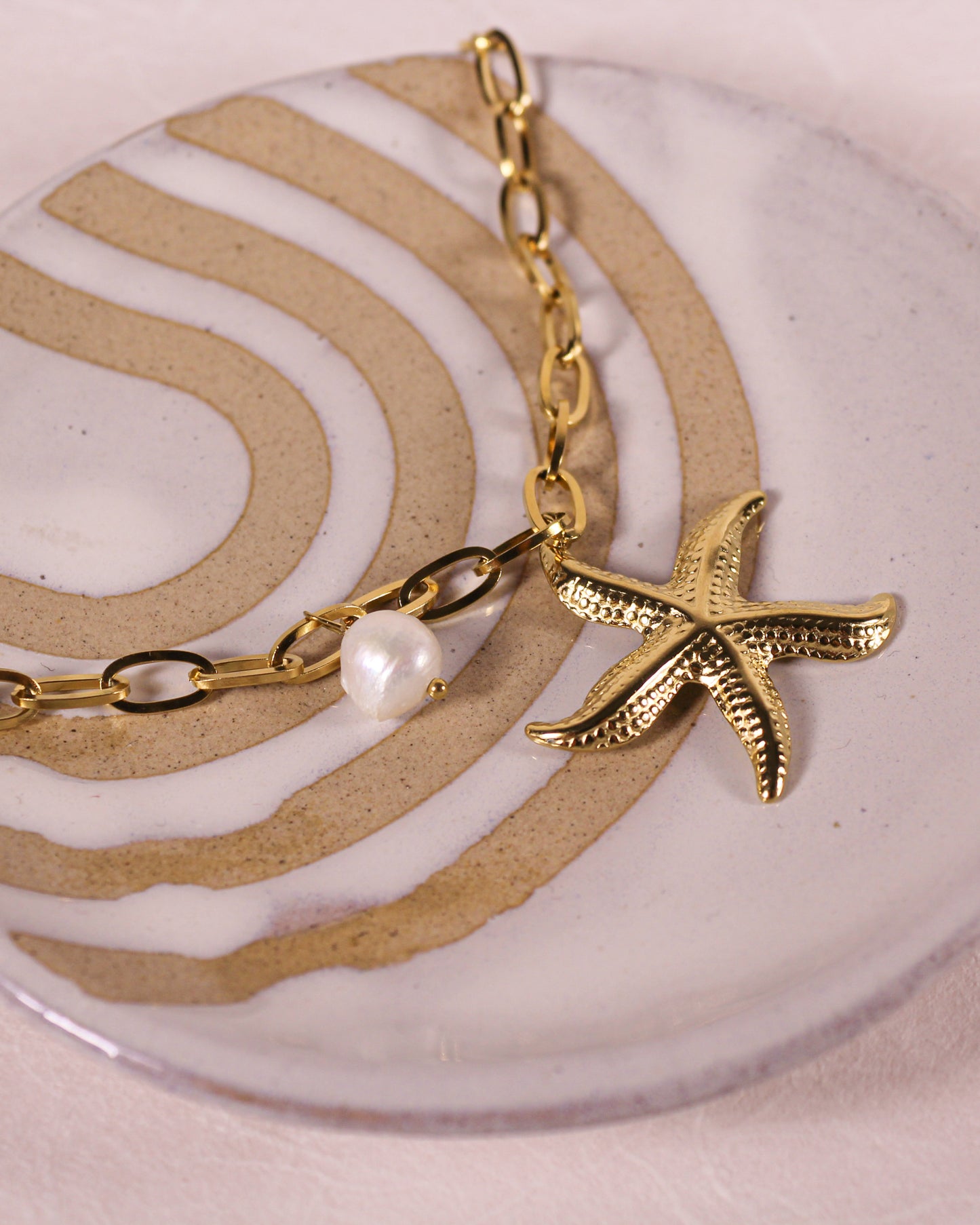 Gold necklace with a starfish charm and pearl on a decorative plate