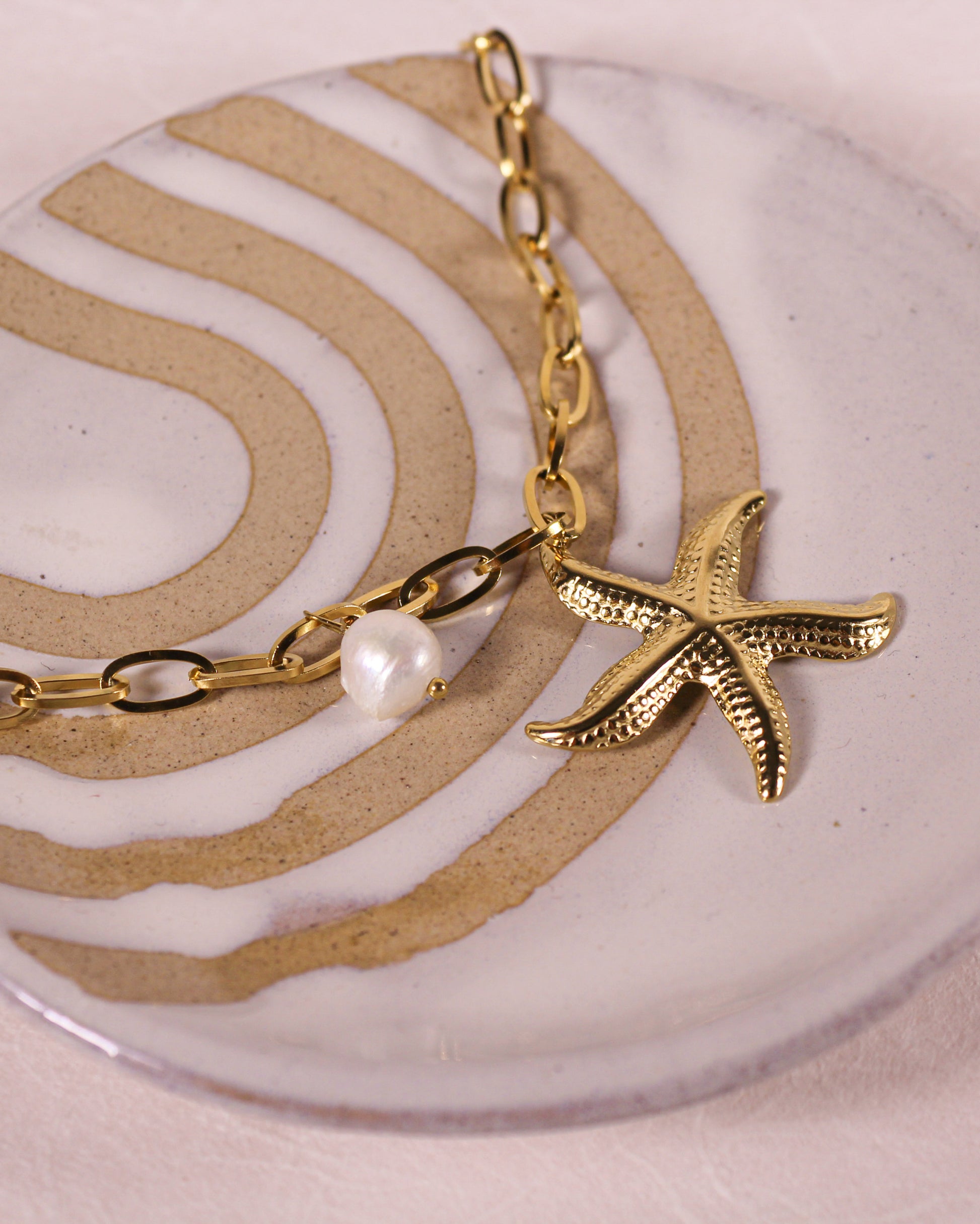 Gold necklace with a starfish charm and pearl on a decorative plate
