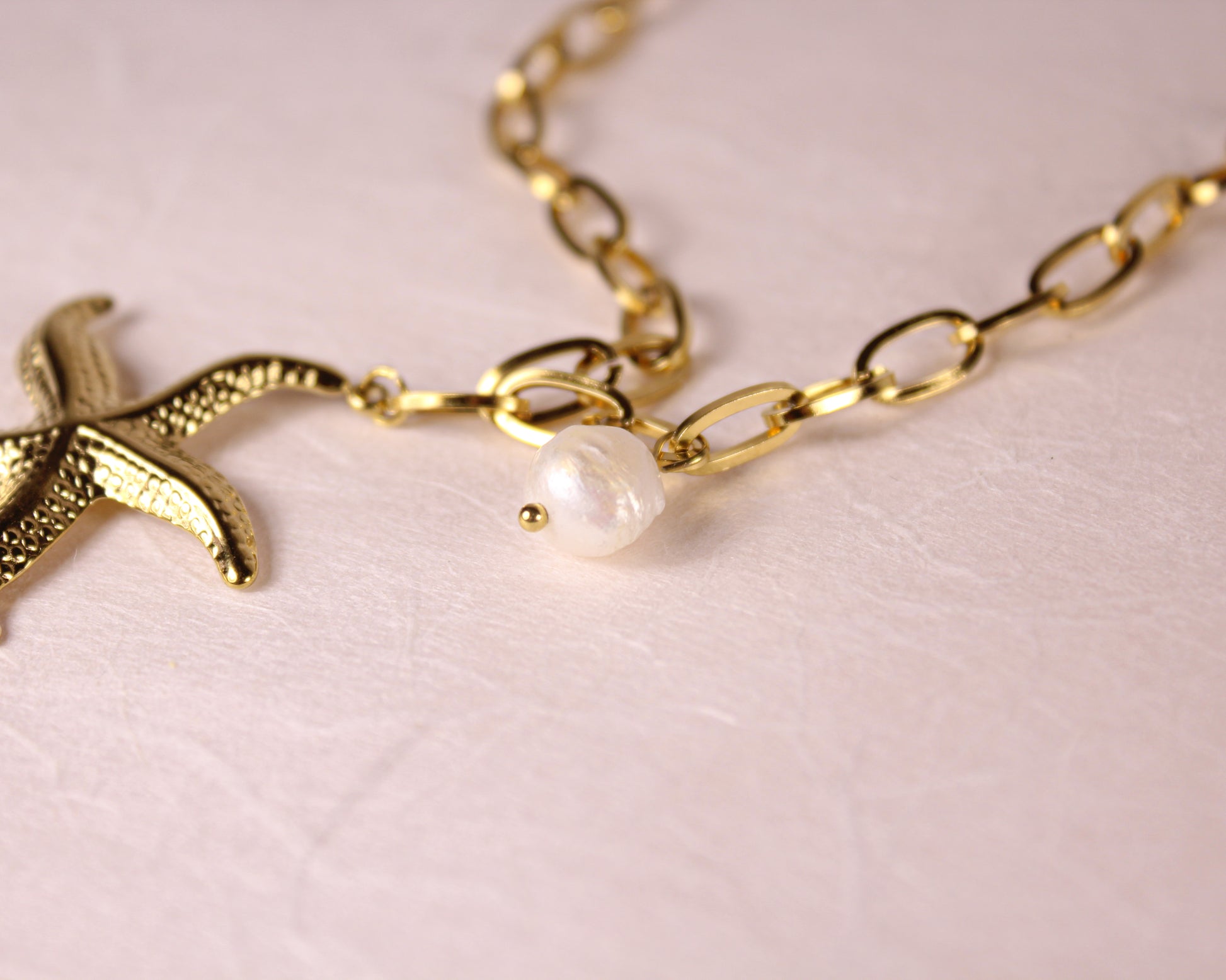 Gold chain necklace with starfish and pearl charm on a light pink background