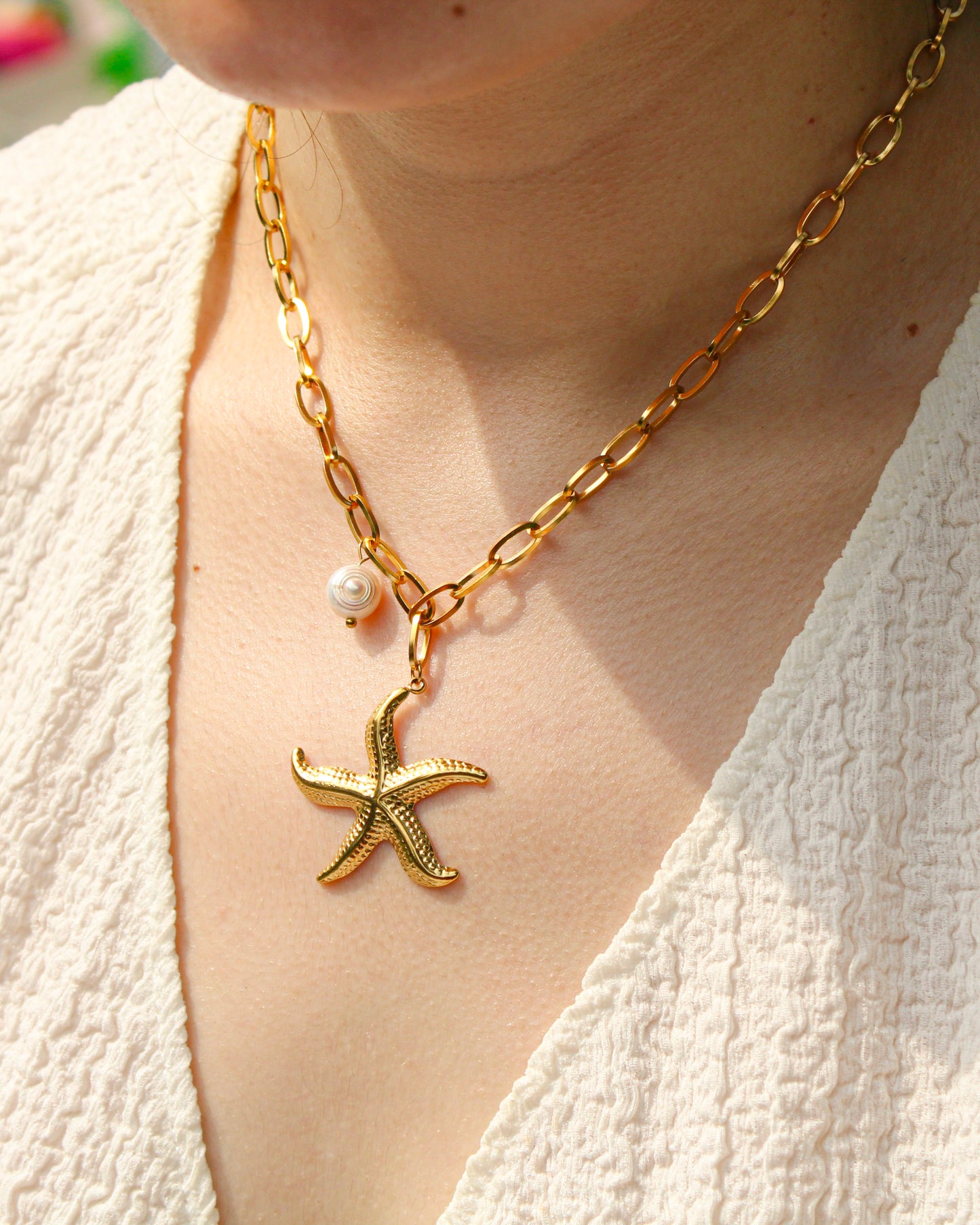 Gold necklace with a starfish pendant and pearl on a person wearing a white top.