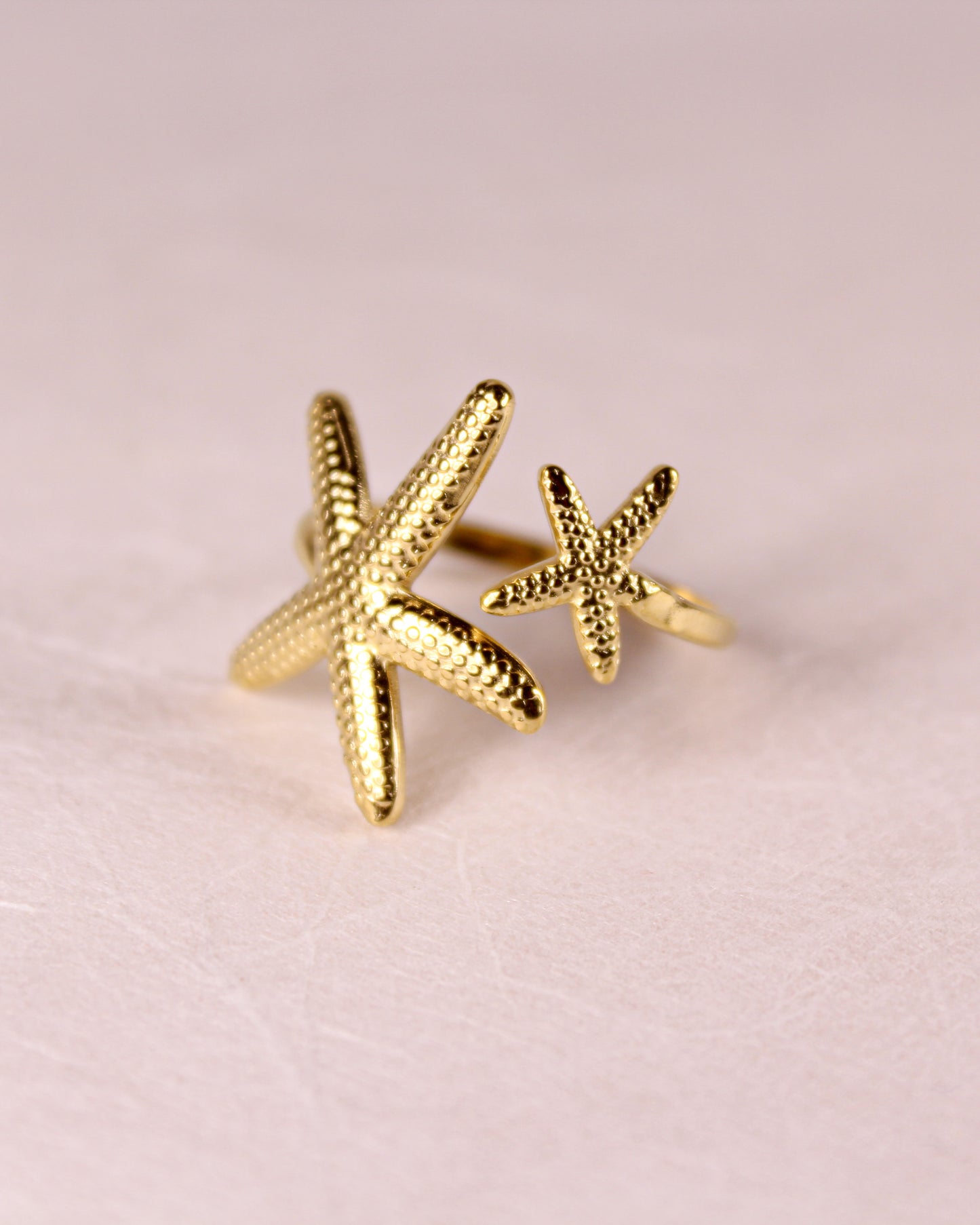 Gold starfish-shaped earrings on a pink background