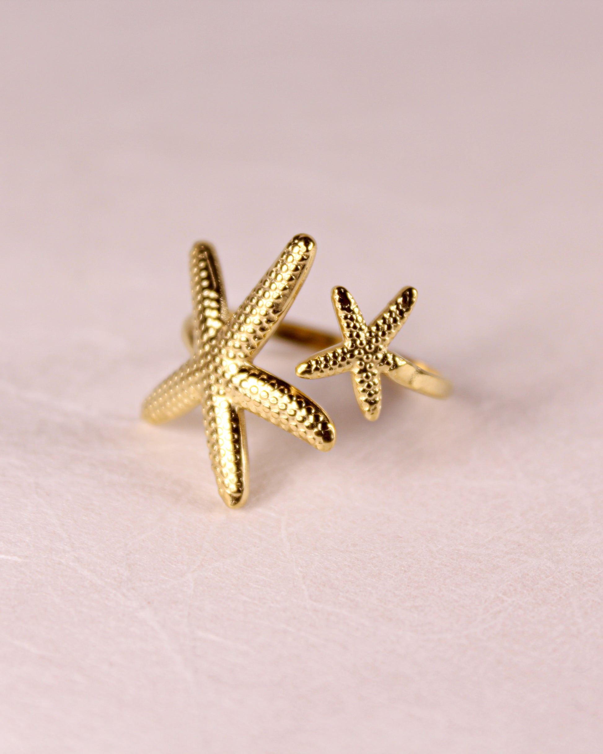 Gold starfish-shaped earrings on a pink background