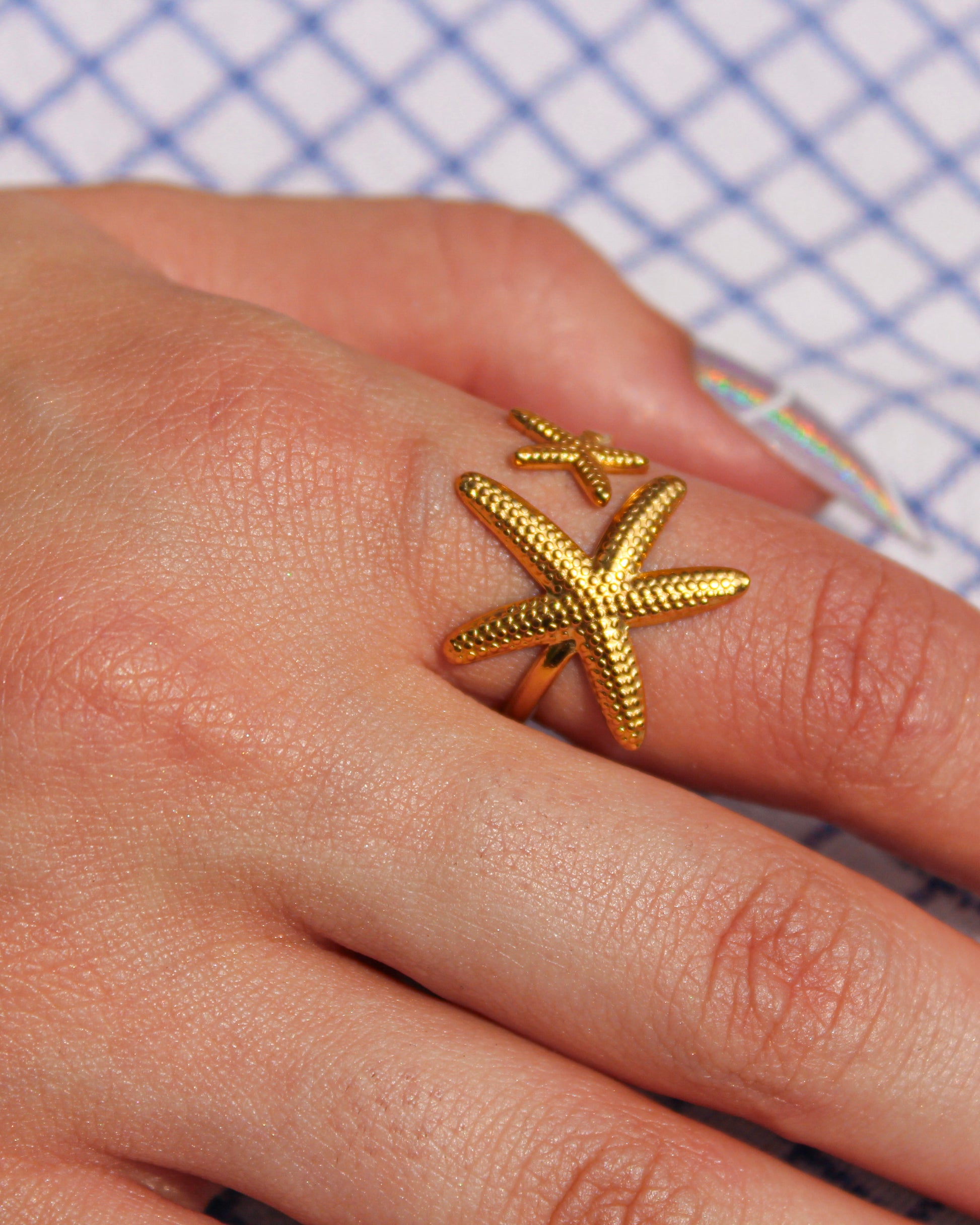 Gold starfish ring on a person's finger with a checkered background